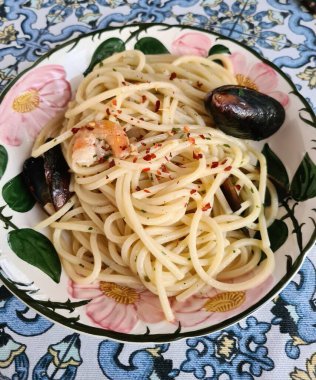 evocative close-up image of a plate of spaghetti with mussels, prawns, parsley and chilli pepper