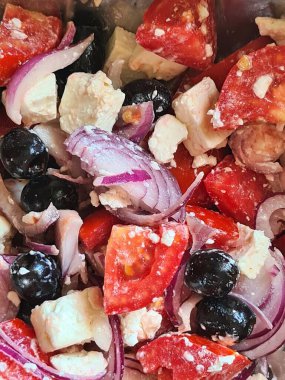 evocative close-up image of a greek based saladtomatoes, feta cheese and onions topped with black olives, oil, salt and chilli pepper