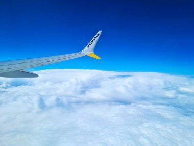 2023.04.17 Milan Malpensa Havalimanı, Ryanair düşük maliyetli havayolu mavi gökyüzü ve beyaz bulutlar arasındaki uçuş safhasında uçağın kanadının yakın çekim görüntüsü