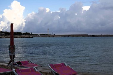 Sicilya 'da dalgalı deniz, bulutlar ve arka planda küçük bir adanın canlandırıcı görüntüsü.