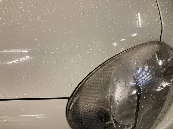 stock image the left-front light of a white car with many raindrops and light bulbs in the indoor parking lot shines on it