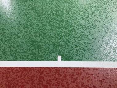 the empty green and red outdoor tennis court with the raindrops all over and the white line at the end of the court