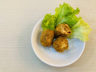 Üç parça kızarmış yengeç köftesi ya da Tayland dilinde beyaz tabakta yeşil salatayla ahşap masaya konmuş Hoi jo pu.