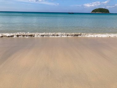 Güzel, pürüzsüz bir kumsal, berrak mavi bir okyanus, inanılmaz dalgalar, bir balıkçı teknesi, küçük yeşil bir ada, denizde iki insan, ve parlak mavi bir gökyüzü.