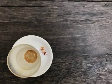 Bir fincan sıcak cappuccino kahveyi bitirmiş. Beyaz tabağındaki oldukça küçük çiçekleri doğal koyu kahverengi ahşap masa üzerinde süslemiş.