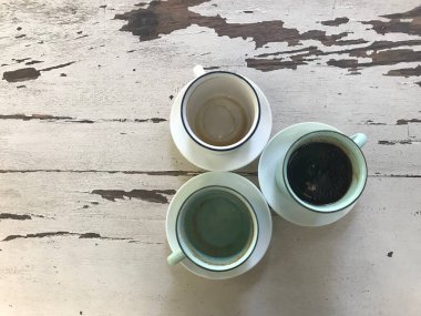 Beyaz seramik bardak bir sade kahve, ve iki bitmiş kahve klasik beyaz-kahverengi ahşap masa üzerinde.