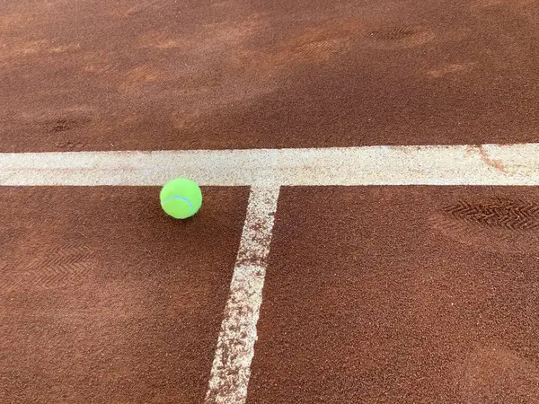 Parlak yeşil tenis topu tam olarak kırmızı kil sahanın ortasına düşüyor.