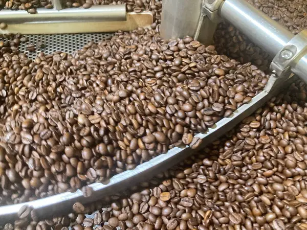 Gümüş kahve makinesinin bulanık görüntüsü kahverengi kahve çekirdeklerini kavuruyor.