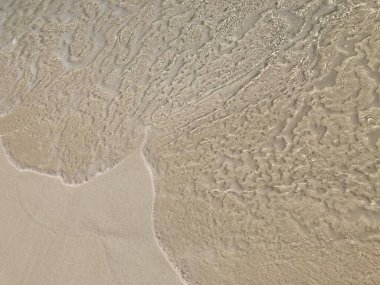 Açık deniz dalgaları kumlu kumsala çarpıyor ve beyin mercanı gibi desenler oluşturuyor.