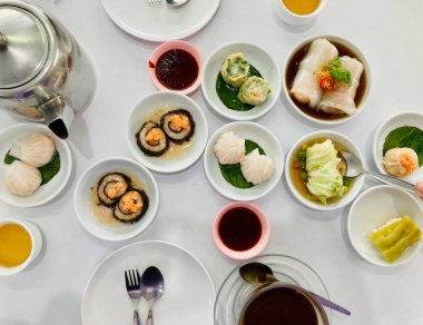 Çin usulü pek çok çeşit, beyaz tabaklar, sıcak Çin çayı ve yerel sade kahveyi beyaz masada buharda pişirdi.