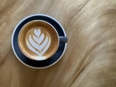 Sıcak cappuccino kahve ve muhteşem zambak çiçekli latte sanat koyu mavi bardakta doğal ahşap masa üzerinde güzel ahşap tahıllı ve çerçevenin sağ tarafında fotokopi alanı olan