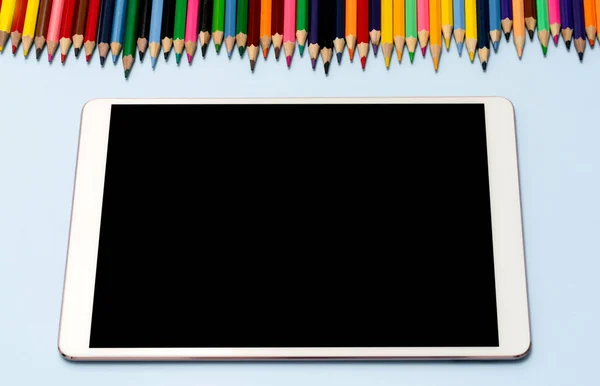A tablet, stylus, and colored pencils lie on the table. View from the top. High quality photo. The concept of online education, training, private drawing and design lessons.