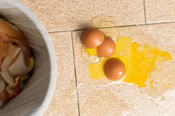 dustbin with organic waste, waste sorting concept. Broken eggs on floor, yolks spilled
