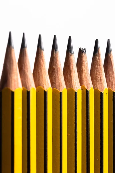 Line of pencils on white background with one pencil having a broken tip