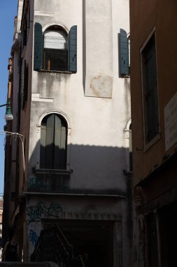 Uzun tarihi binalar, kemerli pencereler ve gölgeli geçitlerin üstündeki yeşil panjurlar kulesi..