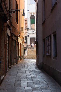 Dar bir Venedik ara sokağının sonundaki taş merdivenlerde yürüyen biri..