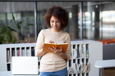 Young African American female teacher is preparing for the lesson. Woman notes, preparing for exams in university library, education at school