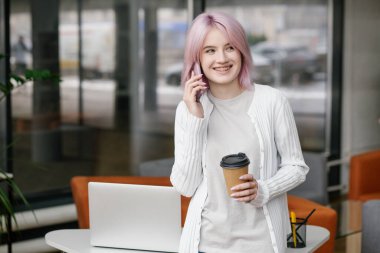 Young attractive successful woman programmer or student uses a mobile phone and takes a coffee break at the modern office.