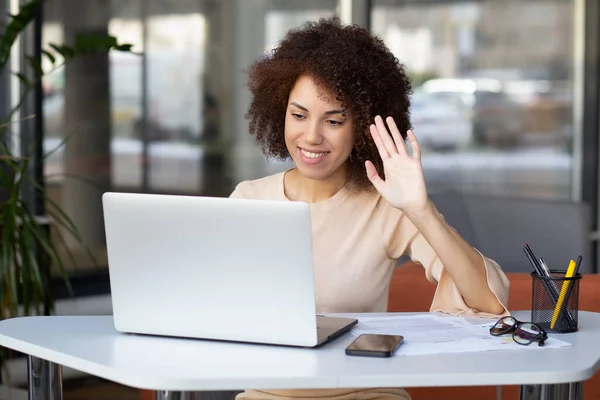 Excited african american female entrepreneur having video call on laptop, waving hand to webcam. Smiling african american woman makes a video call on laptop
