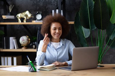 Afrikalı Amerikalı kadın, modern ofiste dizüstü bilgisayarla konuşurken parmaklarıyla aşk jesti yapıyor. Ofisteki genç iş kadını. 