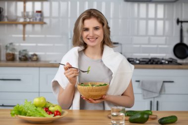Evdeki mutfakta salata yiyen genç ve güzel bir kadın. Sağlıklı salata yiyen güzel bir kız, sağlıklı bir yaşam tarzı.