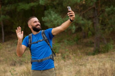 Mutlu sakallı adam ormanda cep telefonuyla video görüşmesi yapıyor..
