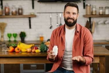 Sakallı bir adam kavanozdan eline hap döker ve gülümser. Hap alma kavramı. Haplar, vitaminler, beslenme malzemeleri.