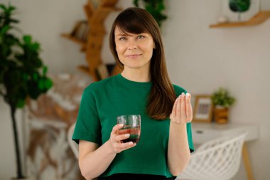 Elinde vitamin hapı ve su tutan gülümseyen kadın, sağlığa odaklanıyor. Sağlıklı bir yaşam tarzı, kişisel bakım ve sağlık rutini kavramı.