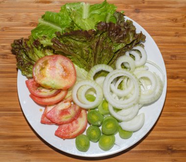 Beyaz bir tabakta kesilmiş domates, marul, soğan ve soğan.