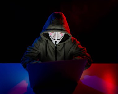 5 Haziran 2022 Novosibirsk, Rusya: Kapüşonlu Anonymous kırmızı ışıkta karanlıkta dizüstü bilgisayarda yazıyor