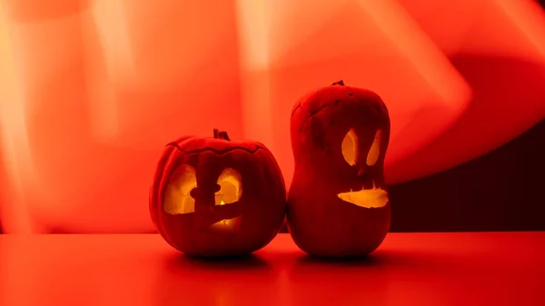 Two jack-o-lanterns glow in the dark on a red background. Halloween decoration