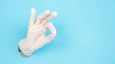 Eldivenli bir kadın, mavi bir kağıttan sarkar ve iyi olduğuna dair bir işaret gösterir.