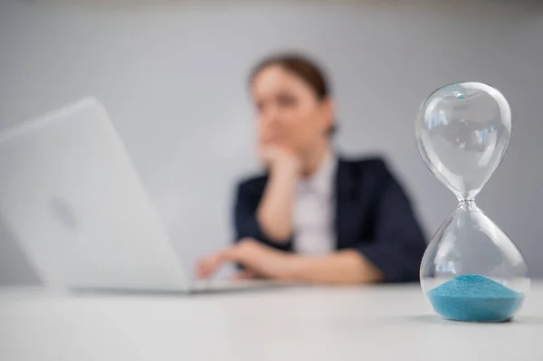 Business woman keeps track of time on an hourglass while working