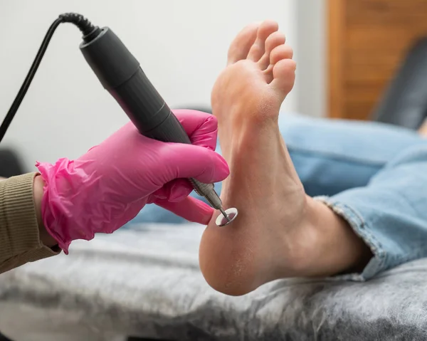 A pedicurist treats the heels of a client using a machine with an abrasive disc in a beauty salon