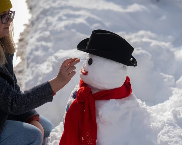 Caucasian woman sculpts a snowman from the snow. The carrot is the place of the nose
