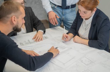 Ofisteki masanın üzerinde planları olan dört meslektaşın ellerinin yakın çekimi. Mühendis ve mimarların beyin fırtınası