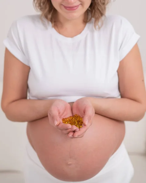 裸の腹を持つ妊婦はビタミンの一握りを保持します 透明な黄金の丸薬 期待する母親のためのビタミンD — ストック写真