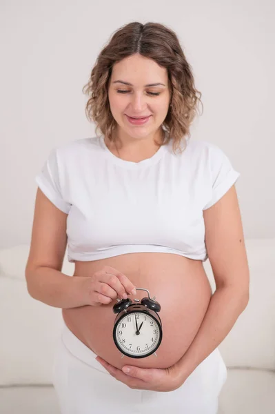 Een Zwangere Vrouw Met Een Naakte Buik Houdt Een Wekker — Stockfoto