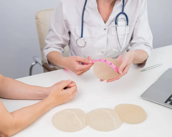 整形外科医は センチメートルテープで乳房インプラントを測定し 女性患者に示す — ストック写真