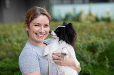 Beyaz, kızıl saçlı bir kadın, pappilion köpeğini açık havada tutuyor. Siyah ve beyaz kıtasal spanyel.