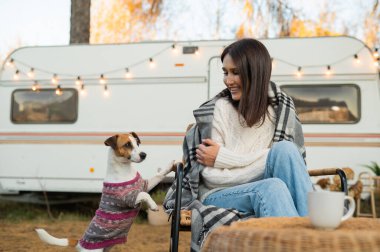 Beyaz kadın hasır bir sandalyede oturuyor sonbaharda bahçesinde bir köpekle battaniyeye sarılı.