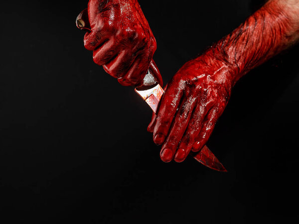 A man wipes a bloody knife with his hand on a black background