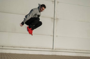 Kapüşonlu beyaz adam elleri dışarıda dizlerinin üzerinde yükseğe zıplıyor.