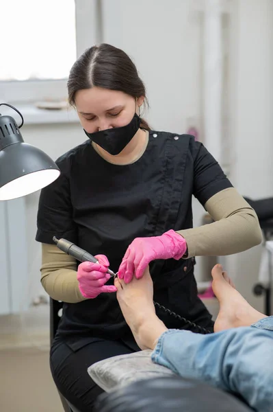 stock image The pedicure master processes the clients foot using an apparatus with an abrasive disc