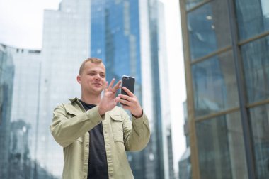 Beyaz adam açık havada akıllı telefondan işaret dili konuşuyor.