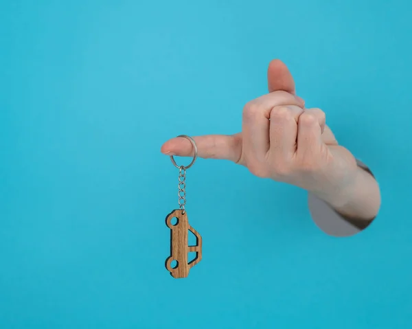 stock image Womans hand holding a wooden keychain in the shape of a car on a blue background