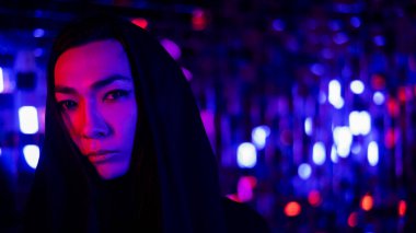 Kapüşonlu bir androjenik modelin yakın plan portresi. Stüdyoda neon ışıklı bir erkek transseksüel.