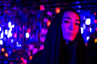 Kapüşonlu bir androjenik modelin yakın plan portresi. Stüdyoda neon ışıklı bir erkek transseksüel.