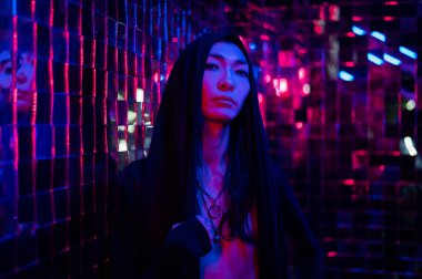 Kapüşonlu bir androjenik modelin yakın plan portresi. Stüdyoda neon ışıklı bir erkek transseksüel.