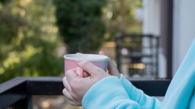 Balkonda sıcak bir şeyler içen bir kadın.